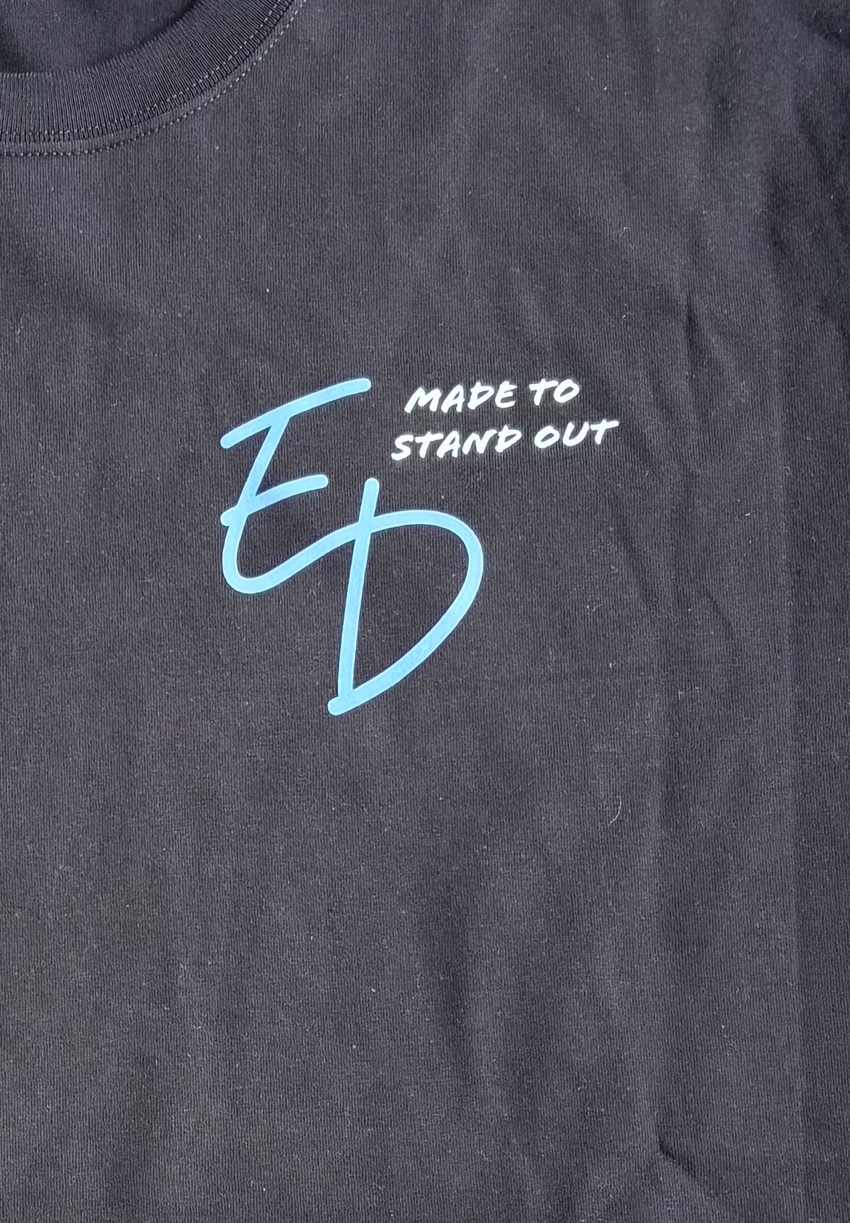 Close-up of the actual pale blue ED print with white Made to Stand Out on a black T-shirt